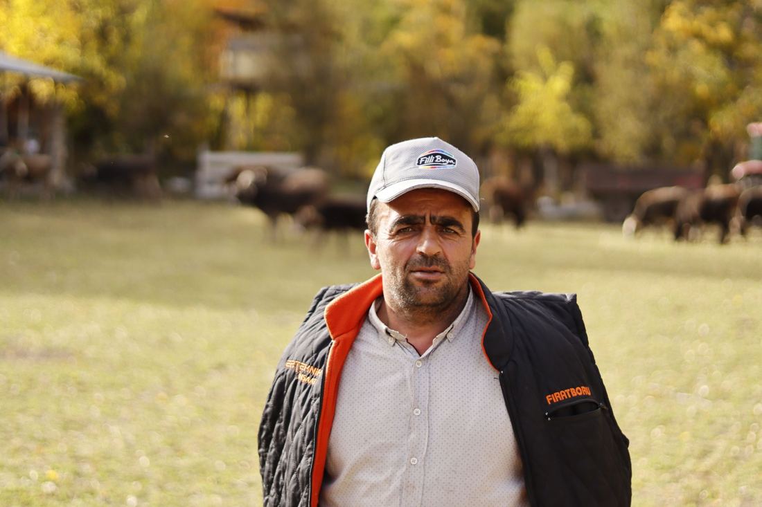Produtor rural de boné no campo, com o rebanho ao fundo