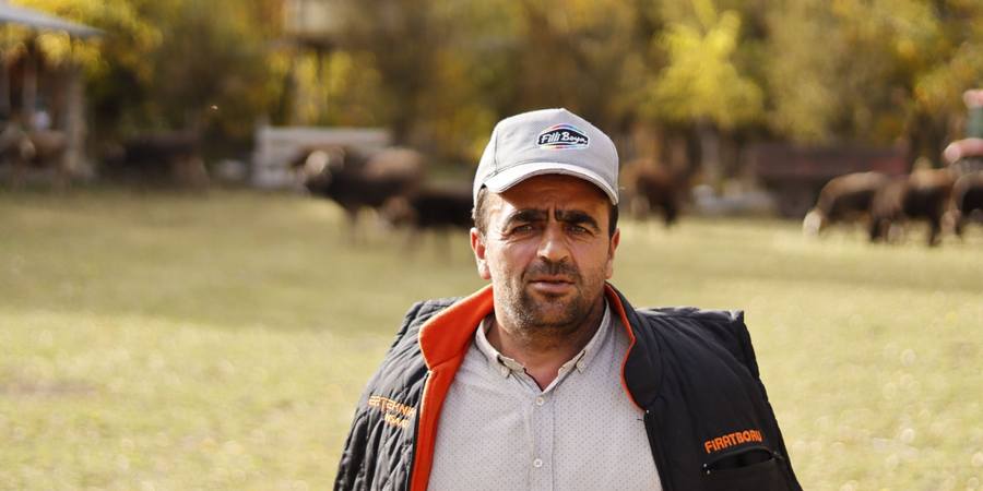 Produtor rural de boné no campo, com o rebanho ao fundo